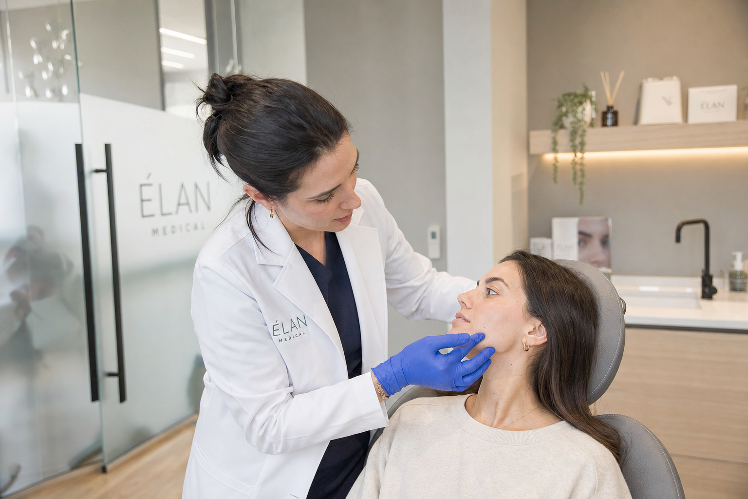 Registered nurse in white lab coat assessing a calm female client's jawline before treatment at KatiFACE